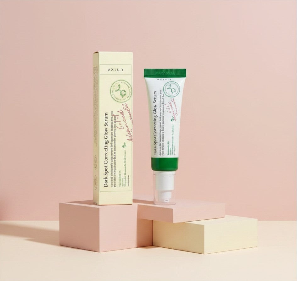 My Glam Room Axis-Y Dark Spot Correcting Glow Serum in a white and green tube with matching box on pastel blocks