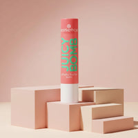My Glam Room essence juicy bomb lip butter balm in a coral tube standing on geometric blocks against a pink background