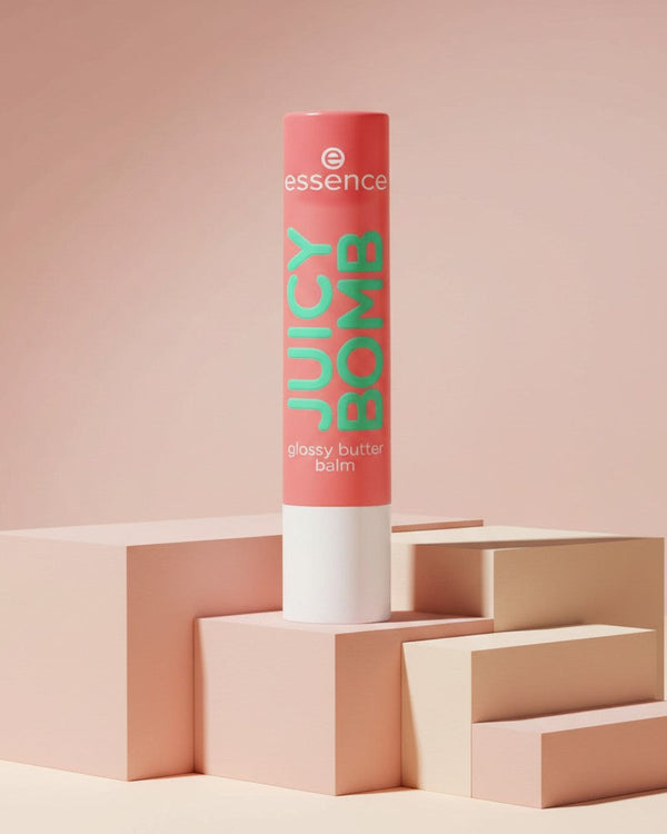 My Glam Room essence juicy bomb lip butter balm in a coral tube standing on geometric blocks against a pink background