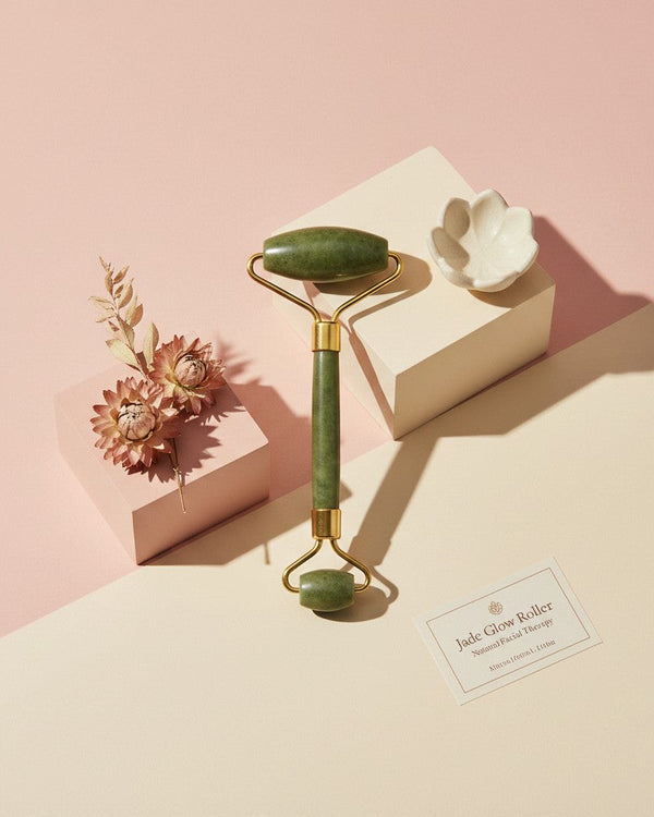 My Glam Room green jade facial massage roller with gold hardware displayed on geometric blocks with dried flowers