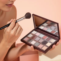 My Glam Room Hudamoji icy nude eyeshadow palette with shimmer and matte shades held by a woman using a makeup brush.