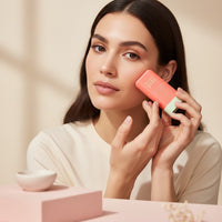 Model applying My Glam Room Pixi On the Glow Stick Blush in a coral shade for a natural, radiant look.