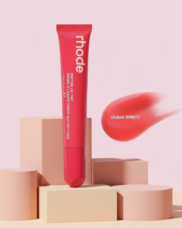 My Glam Room rhode Peptide Lip Tint in Guava spritz shade with a coral pink swatch on a minimalist pedestal display