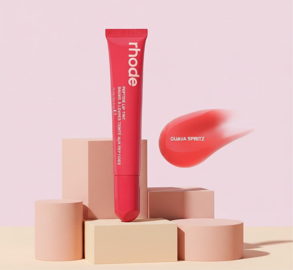 My Glam Room rhode Peptide Lip Tint in Guava spritz shade with a coral pink swatch on a minimalist pedestal display