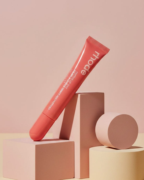 My Glam Room rhode Peptide Lip Tint in Peach Pit, a coral-toned moisturizing lip treatment in a squeeze tube.