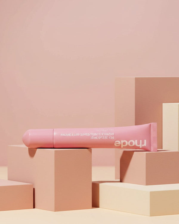 My Glam Room Peptide Lip Tint in Ribbon, a soft pink hydrating lip treatment in a squeeze tube on geometric blocks.