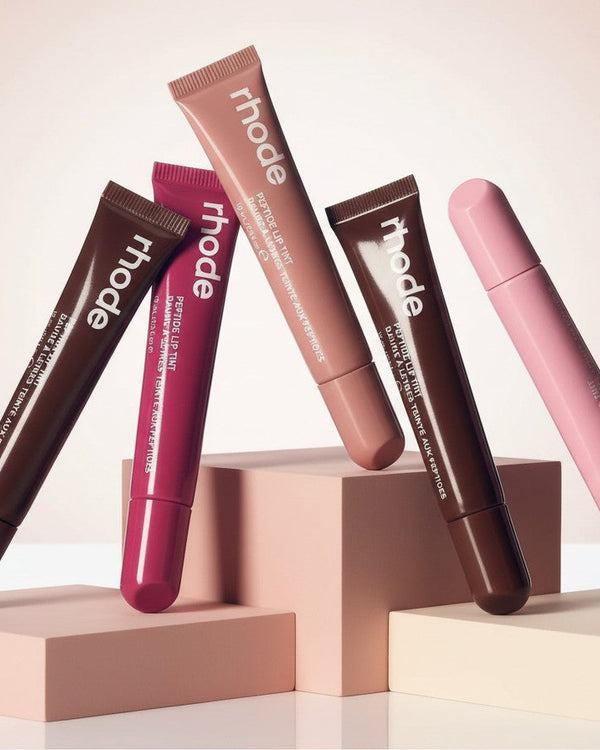My Glam Room Peptide Lip Tint collection featuring five assorted shades in squeeze tubes displayed on geometric blocks